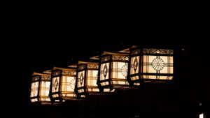 Row of traditional Japanese lanterns casting warm light against dark stone walls.