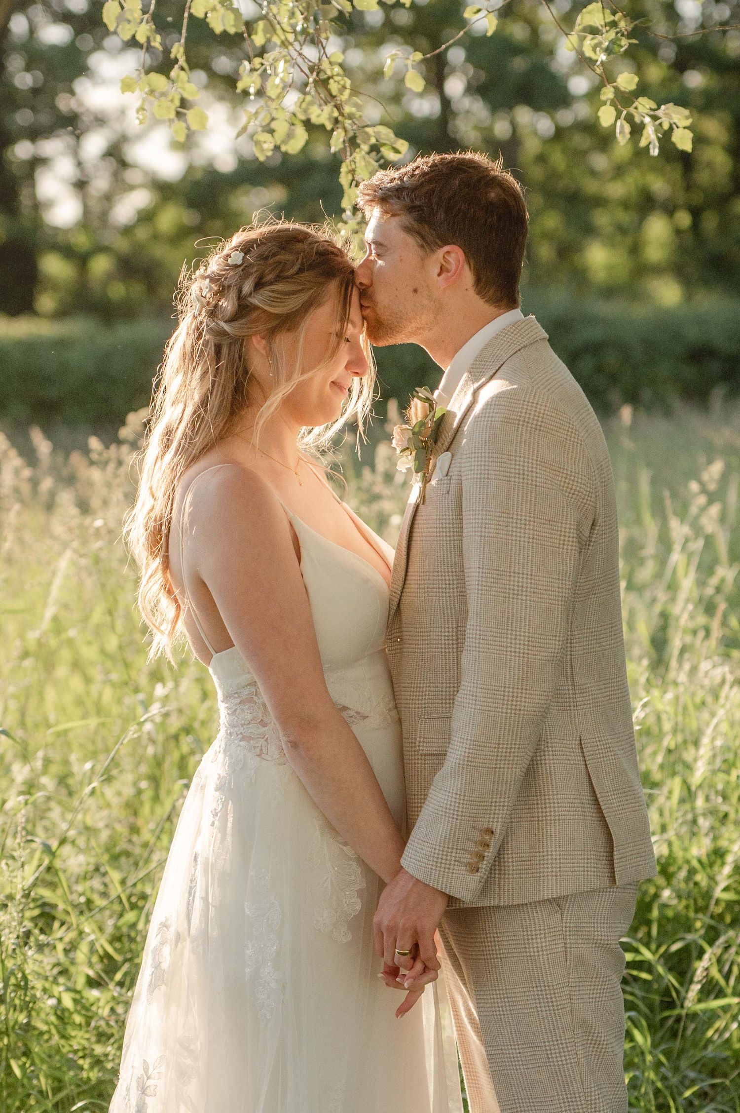 Romantic wedding photo of a couple sharing an intimate moment in a sunlit meadow with soft bokeh background.