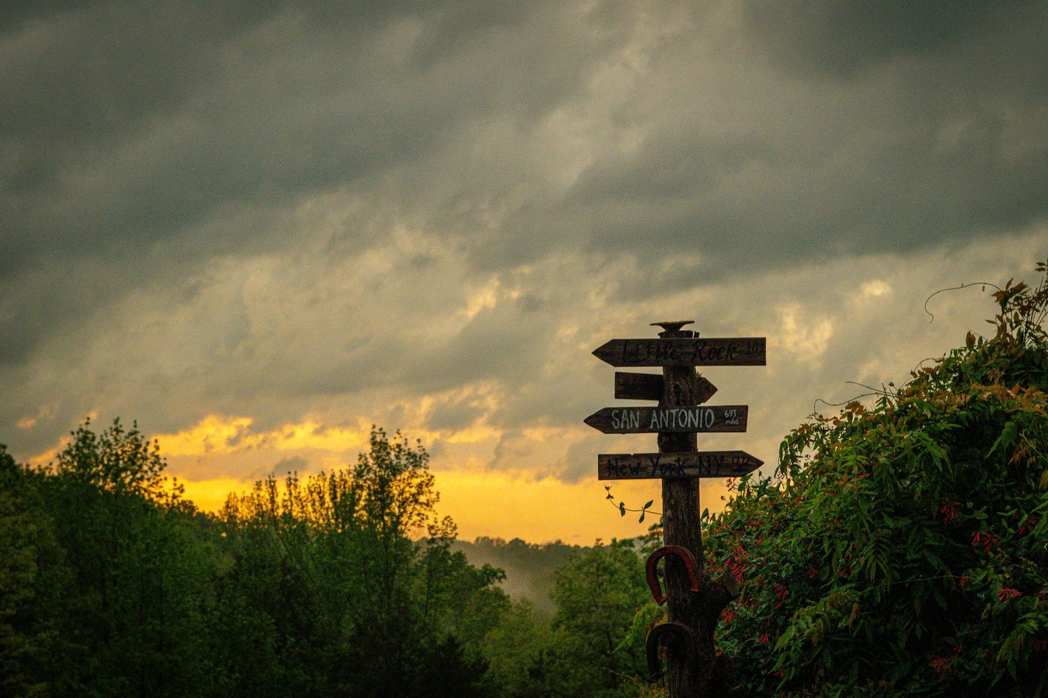 Silhouetted directional sign post against dramatic sunset sky with clouds.