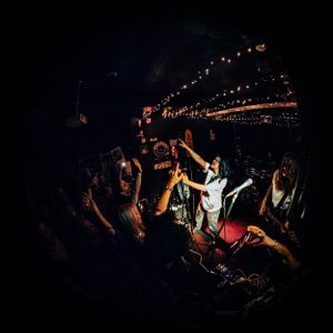 Dark concert venue photo with silhouetted crowd and stage lighting.
