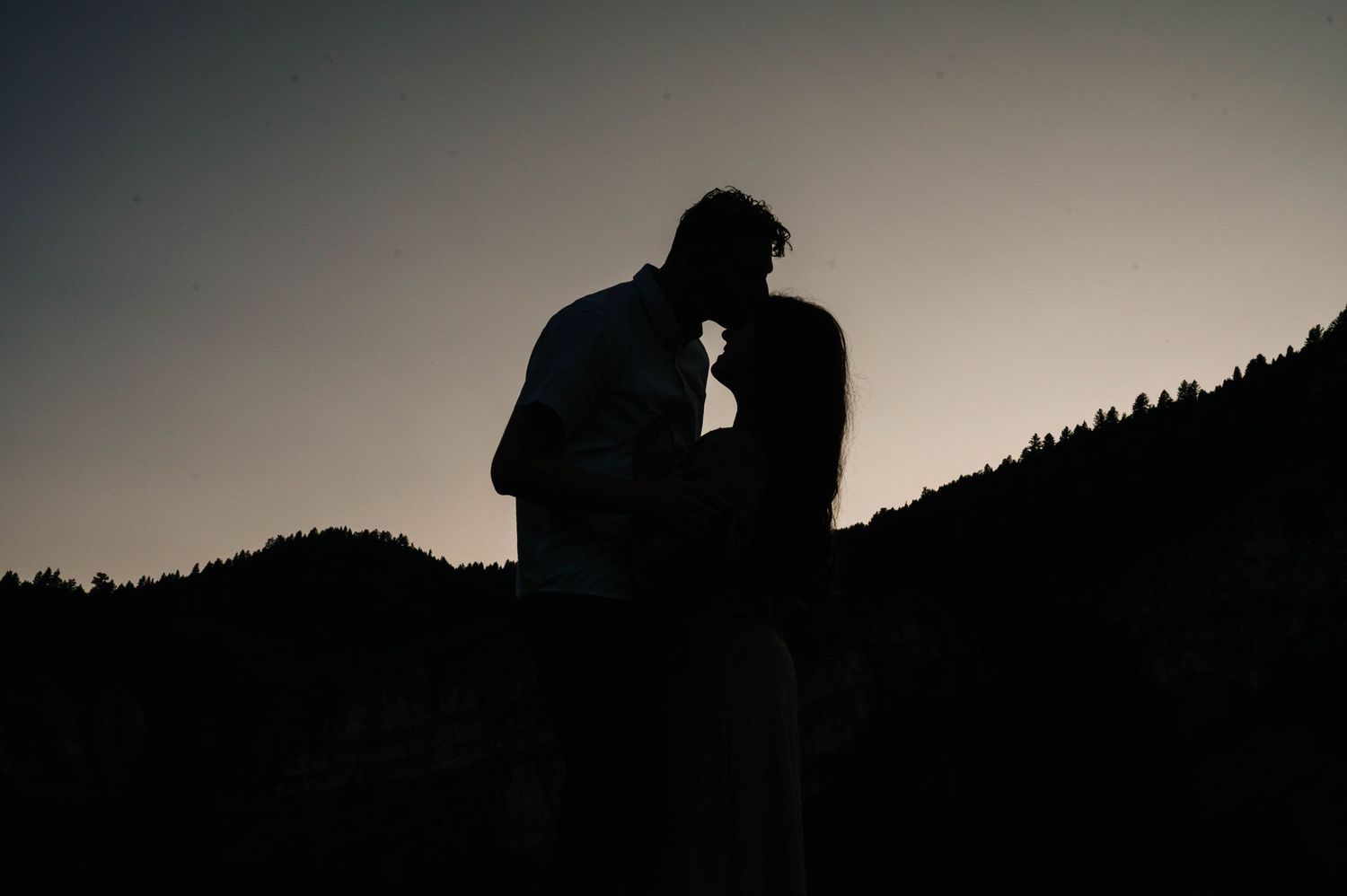 Silhouetted couple embracing against dusky mountain landscape at sunset.