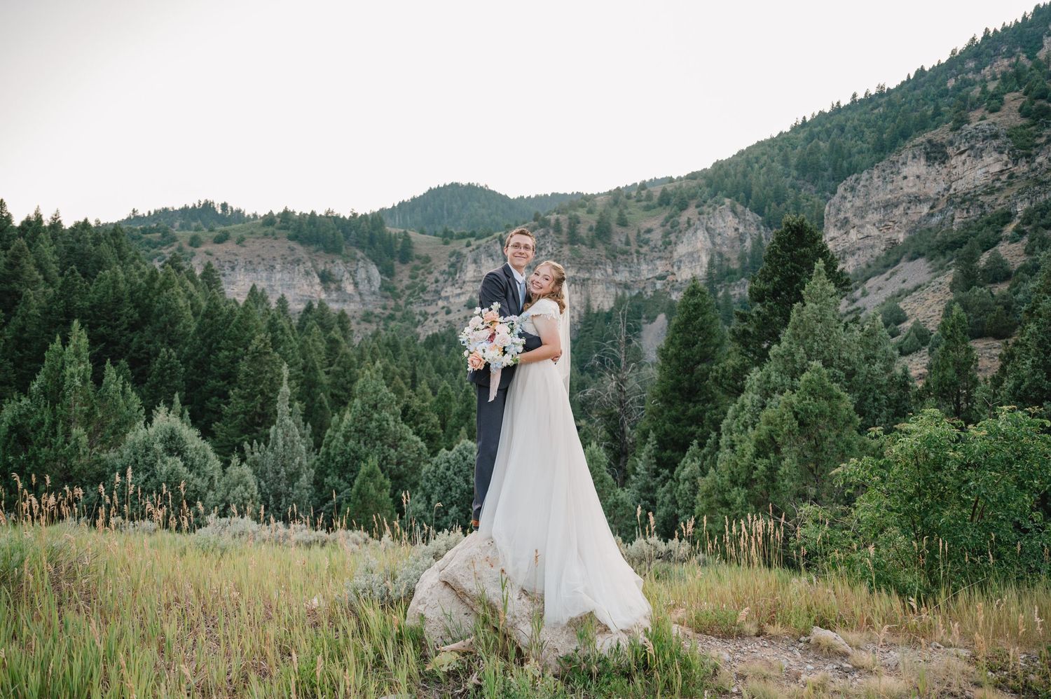 Bride holds colorful bouquet while standing in mountain meadow during wedding portrait session.