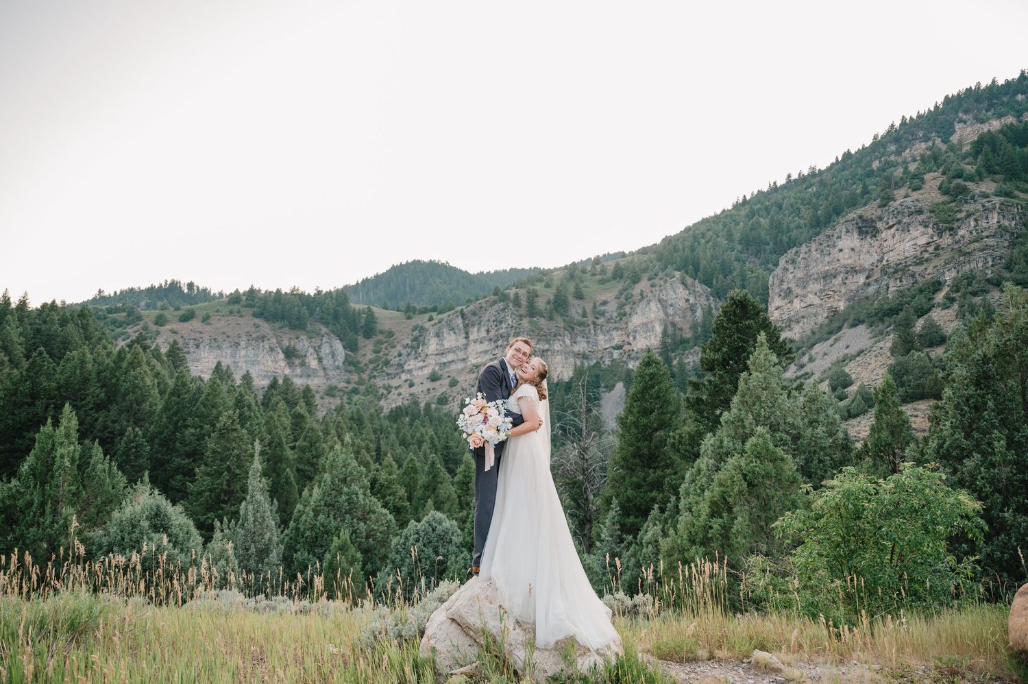A romantic wedding photo featuring a couple in formal attire against a backdrop of rugged mountain scenery.