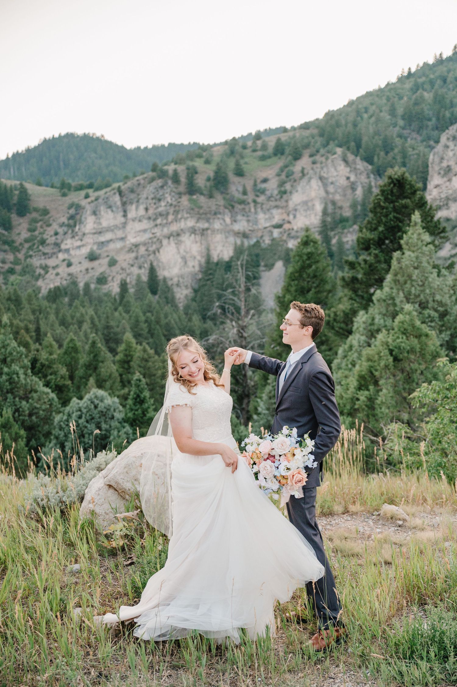 Bride and groom share playful moment while dancing in mountain meadow during wedding portraits.