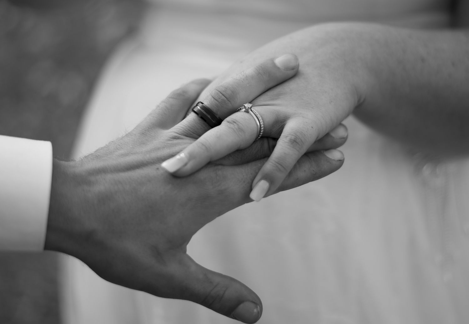 Close-up black and white image of two hands touching tenderly, with one hand placing a ring on the other.