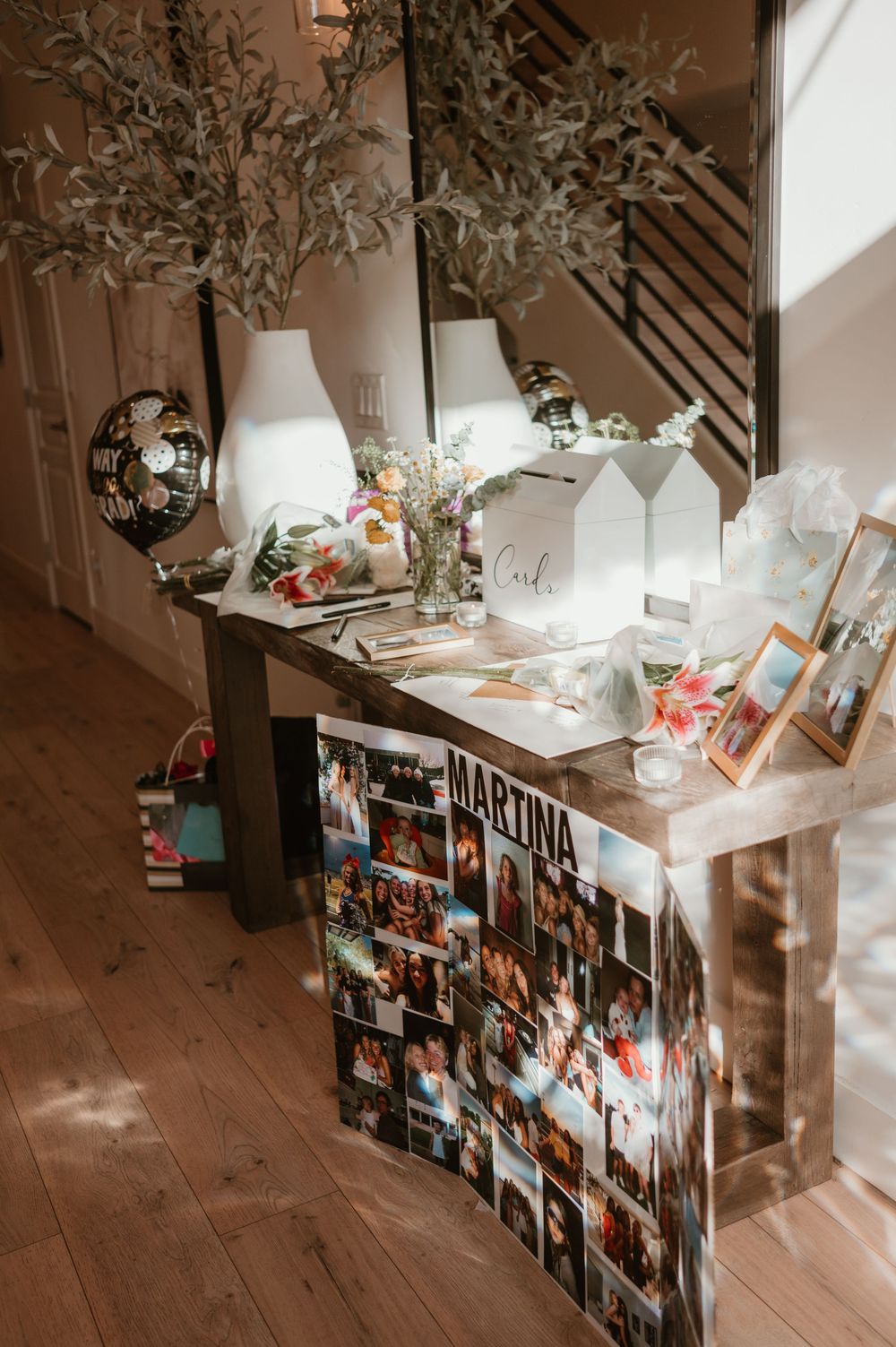 Decorative console table with white lamps, vases, and a collage of photographs displayed below.