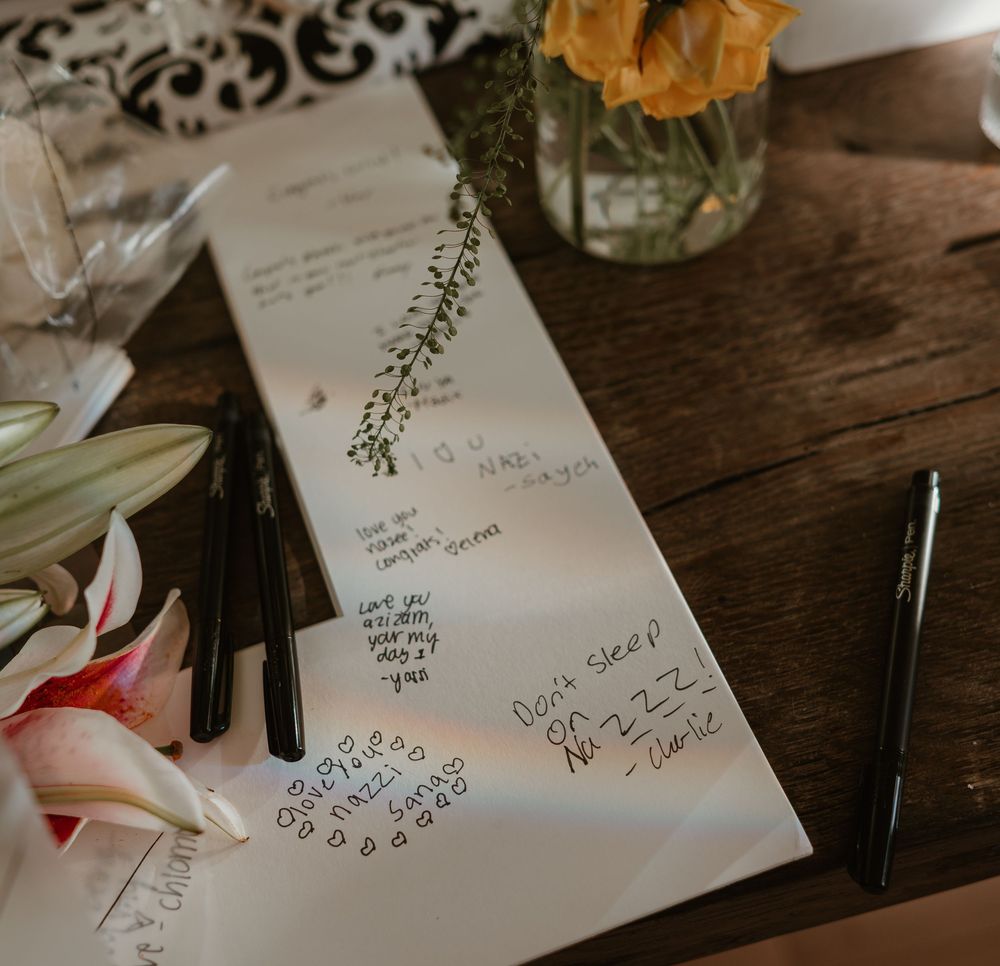 Handwritten notes and signatures on paper with a glass vase and flowers on a rustic wooden table.