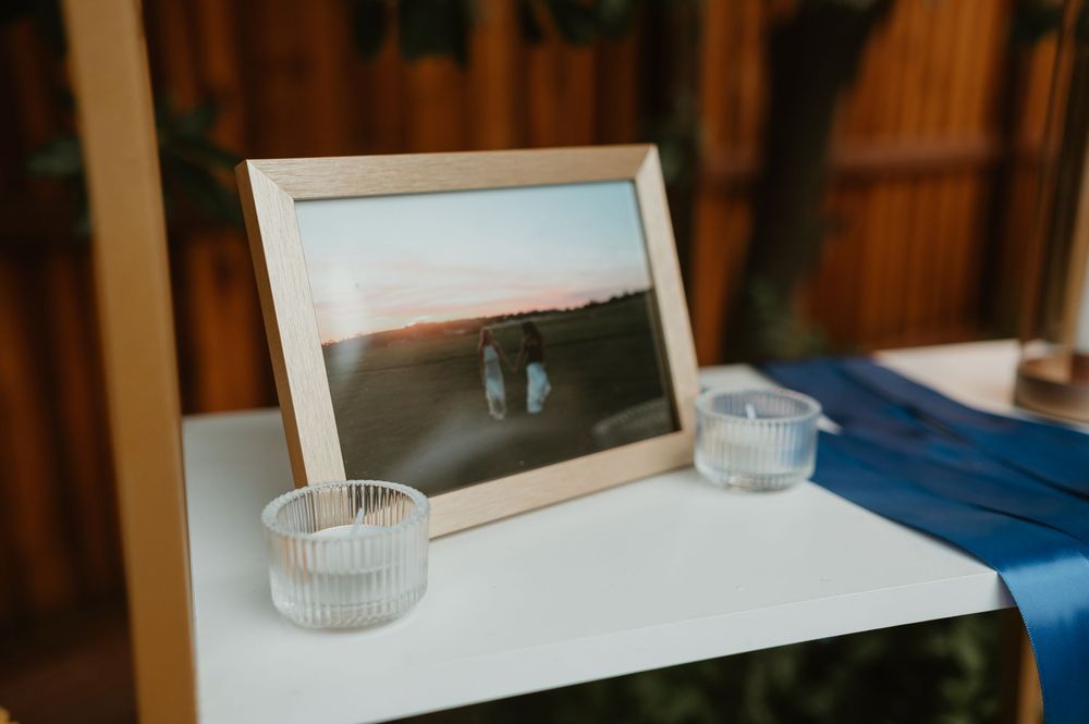 A framed black and white photograph sits on a white surface with two glass tea light holders beside it.
