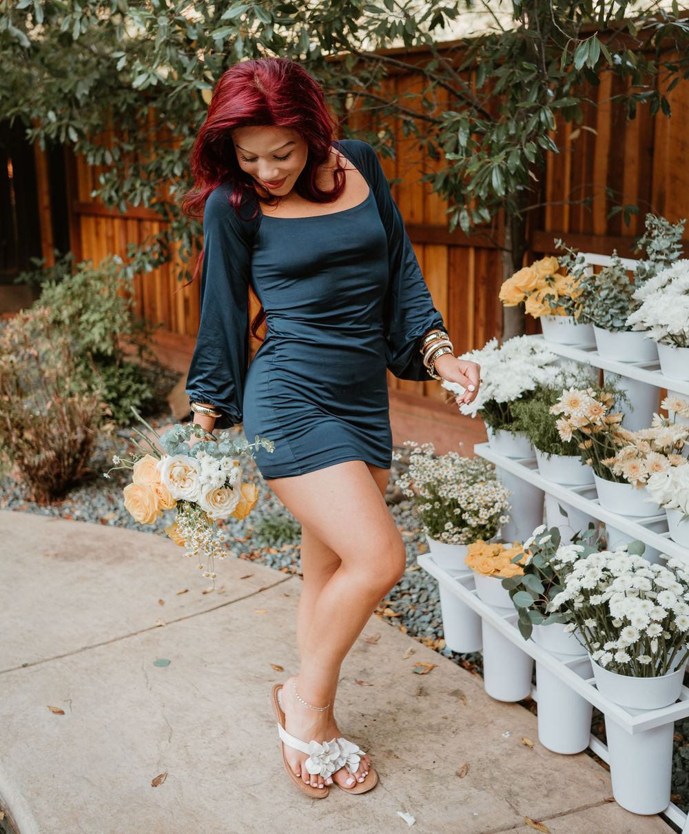 Close-up view of blue dress and sandals against a garden backdrop with white potted flowers.