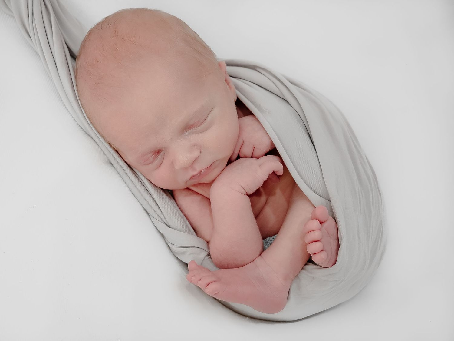 Sleeping newborn wrapped in soft grey fabric during professional photography session.