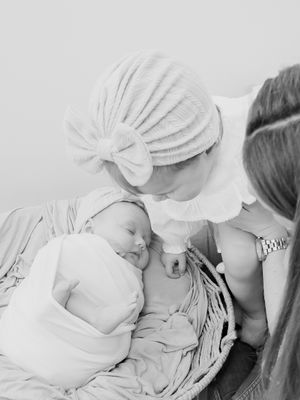 A sleeping newborn in white swaddle rests peacefully in a woven basket.