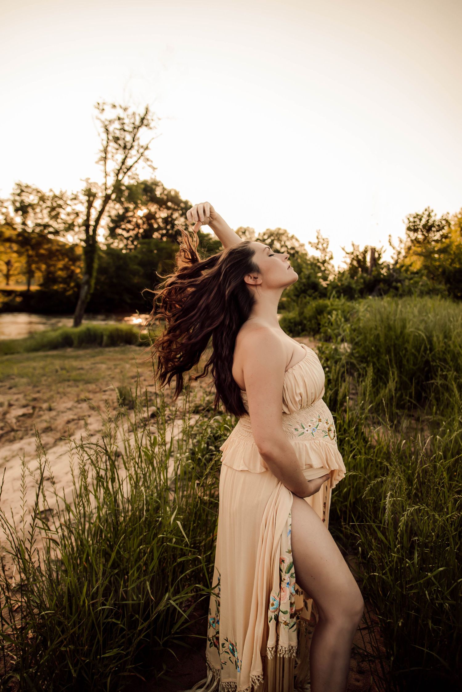 Ethereal maternity portraits in a golden field during sunset wearing a flowing beige dress.