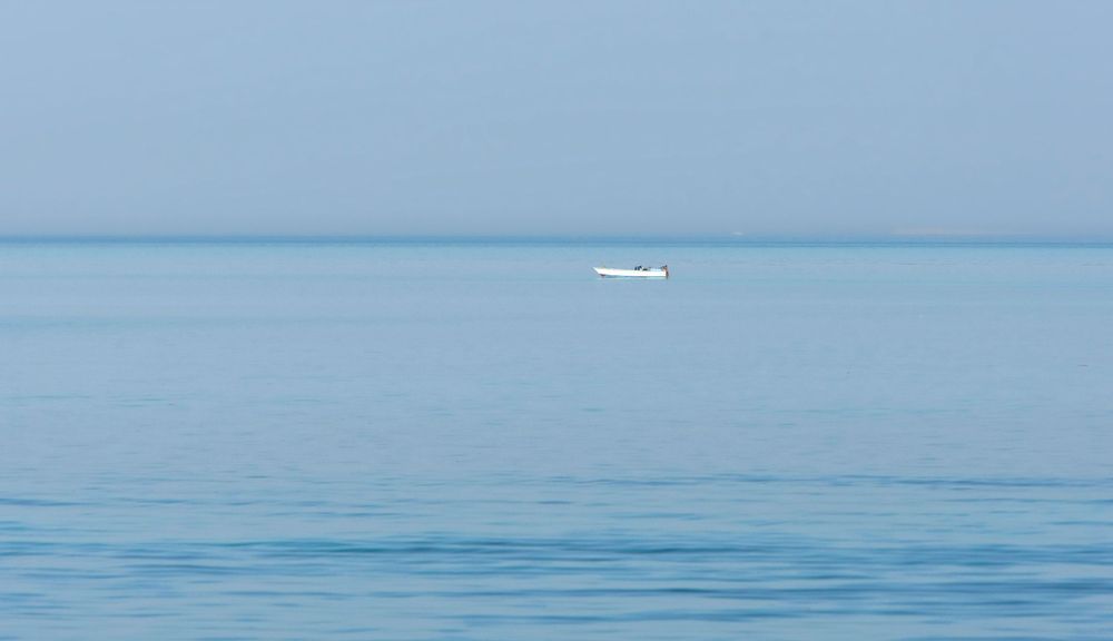 A small white boat floats on calm blue waters of a tranquil ocean.