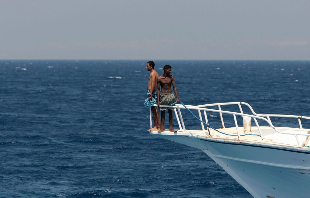 Two people standing on bow of yacht in open ocean waters.