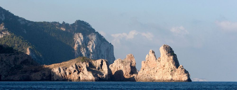 Dramatic rocky coastline with towering limestone formations jutting out into the blue Mediterranean Sea.