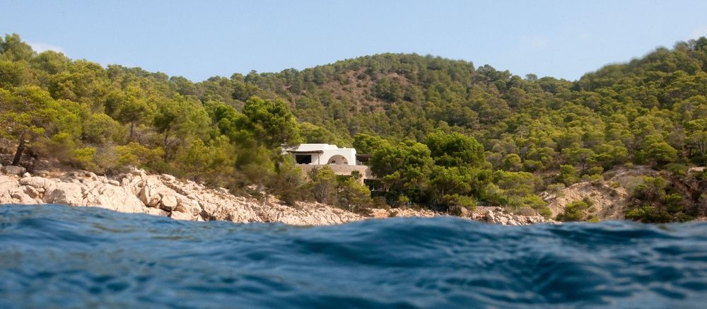 White villa nestled among green hills overlooking turquoise Mediterranean waters.