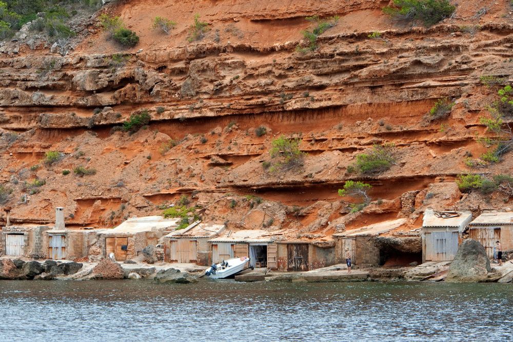 Ancient boat storage caves carved into orange limestone cliffs by the Mediterranean Sea.