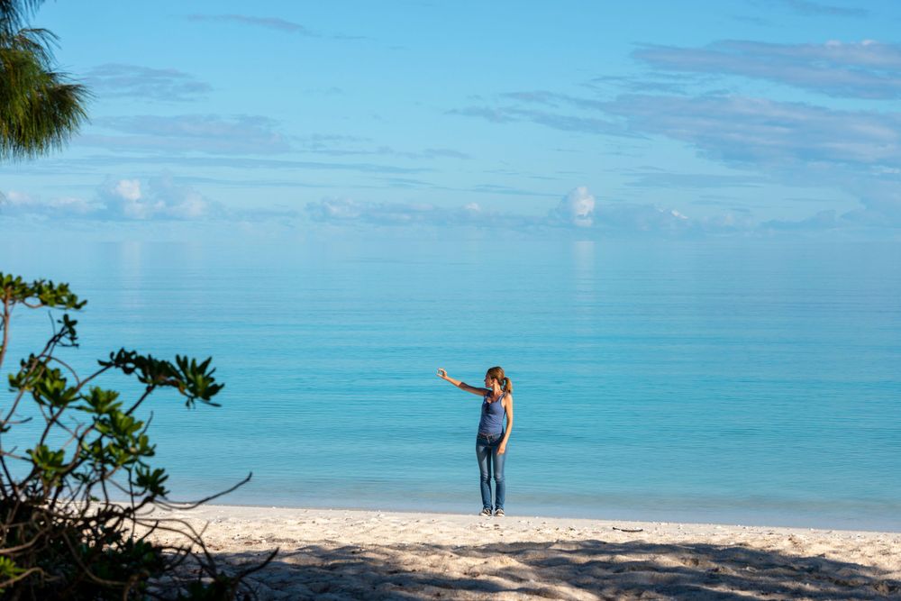 Silhouetted figure stands on pristine beach overlooking brilliant turquoise waters.