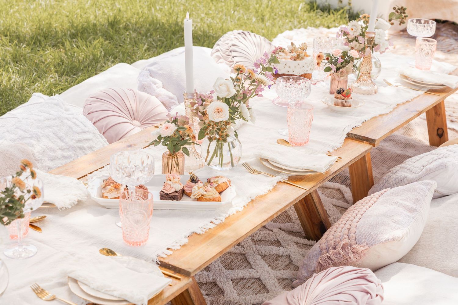 Elegant outdoor table setting with pink pillows, flowers and golden accents.