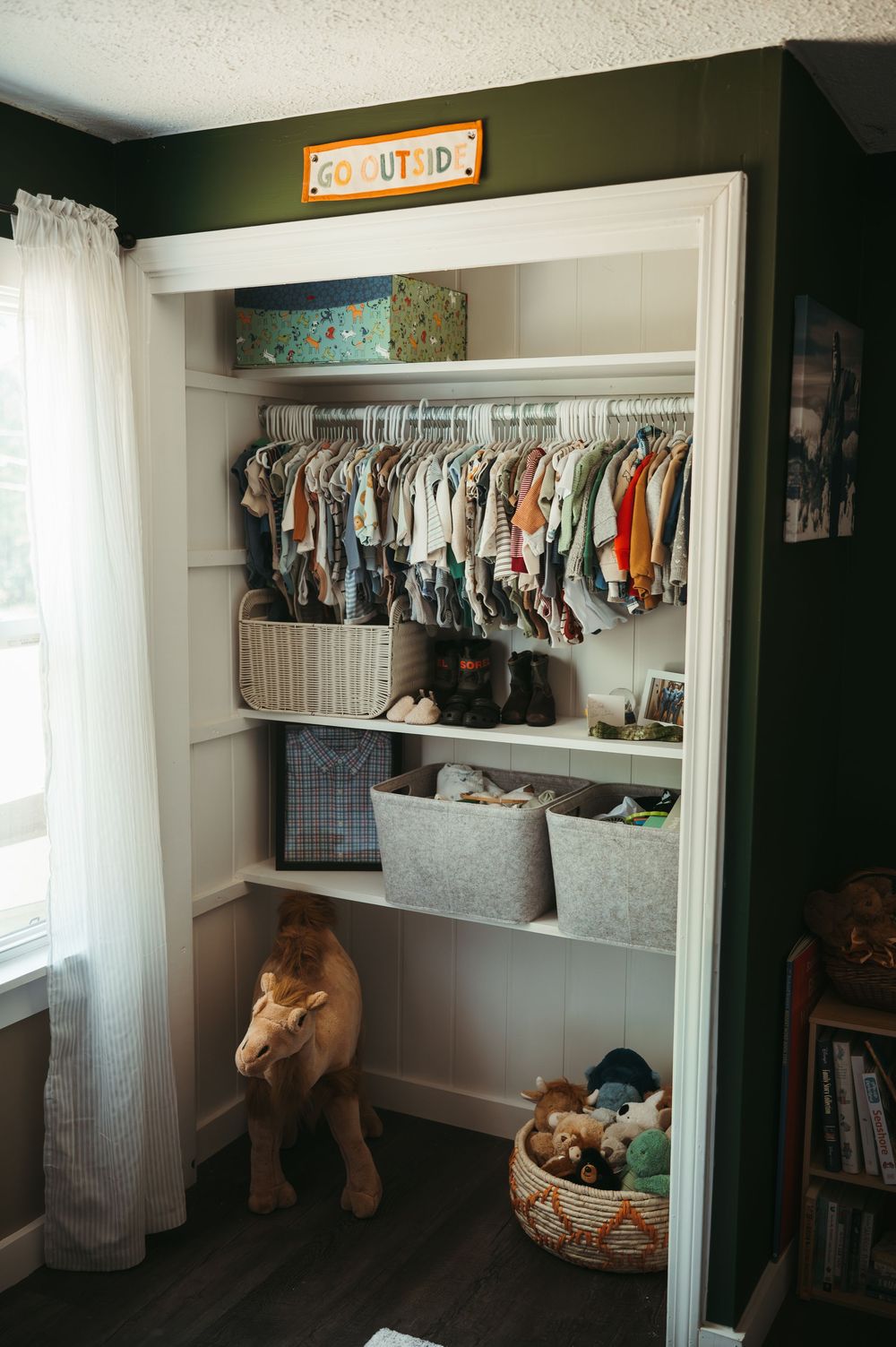 Organized nursery closet with hanging baby clothes, wicker baskets, and a stuffed lion toy on dark hardwood floors.
