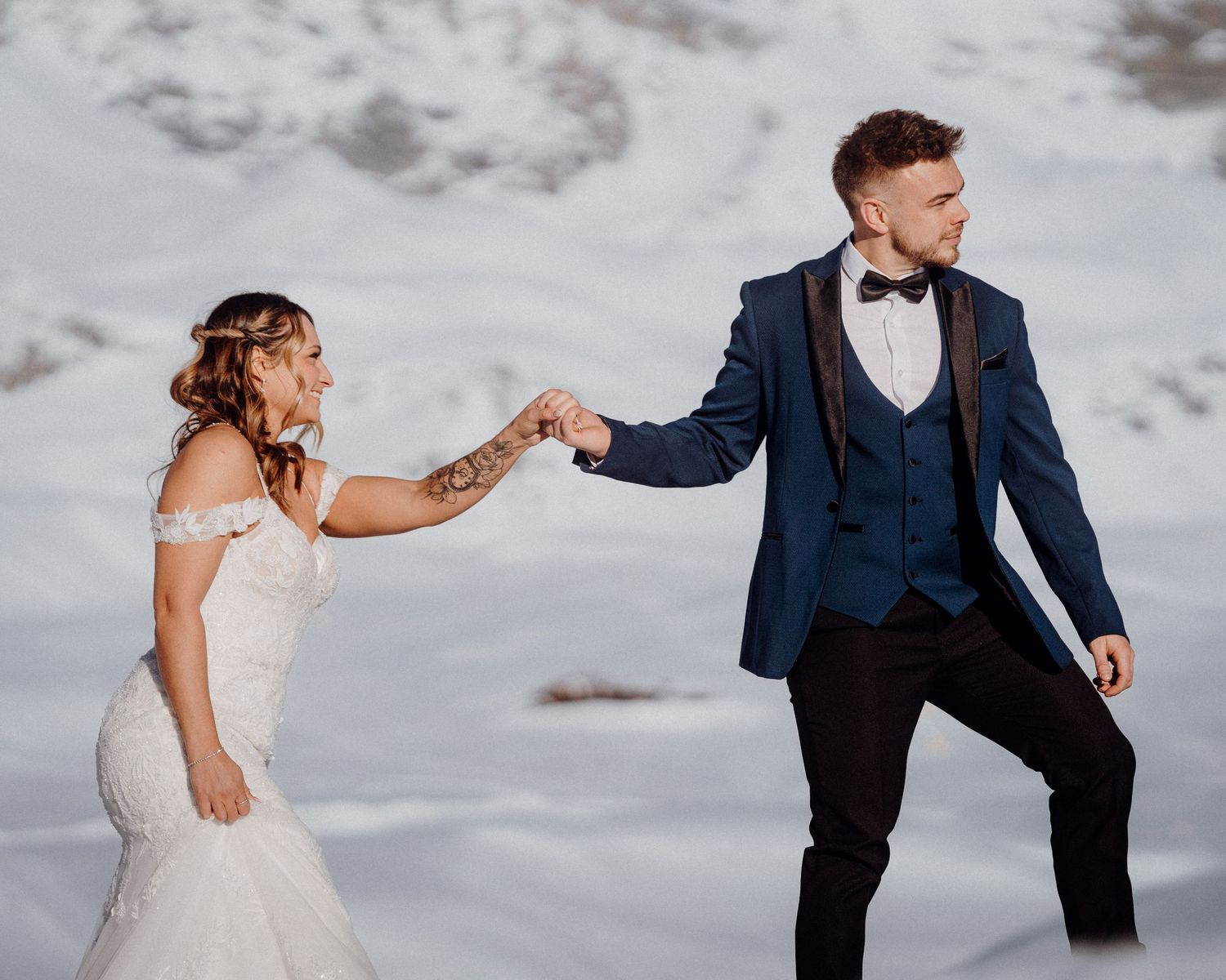 Dancing couple in wedding attire against snowy mountain backdrop.