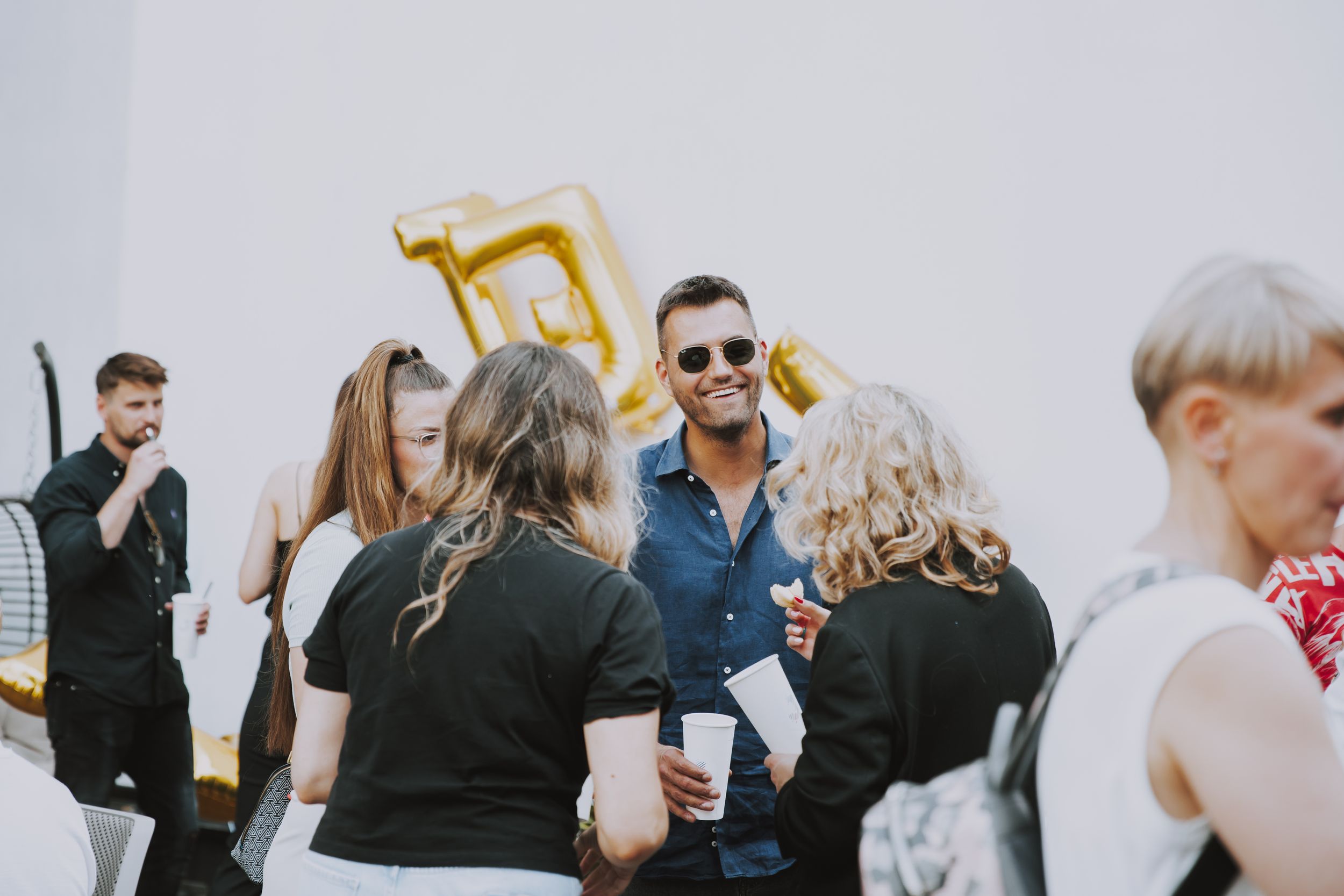 A casual outdoor gathering with people enjoying drinks and conversation on a sunny day.