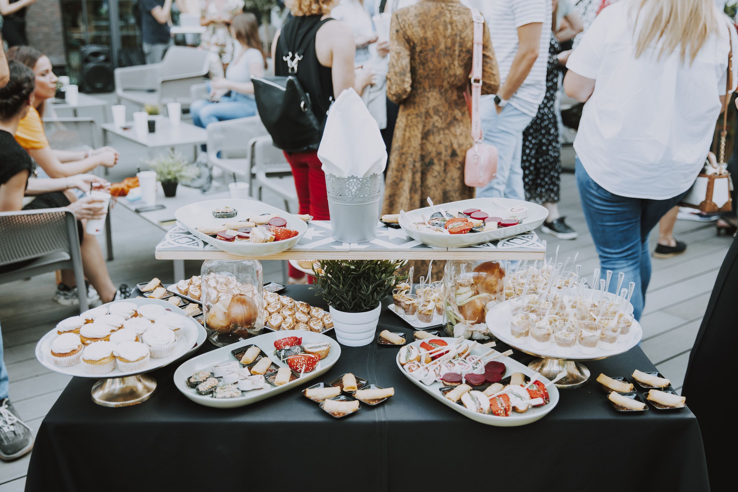Buffet table with various appetizers and desserts on white plates with black tablecloth.
