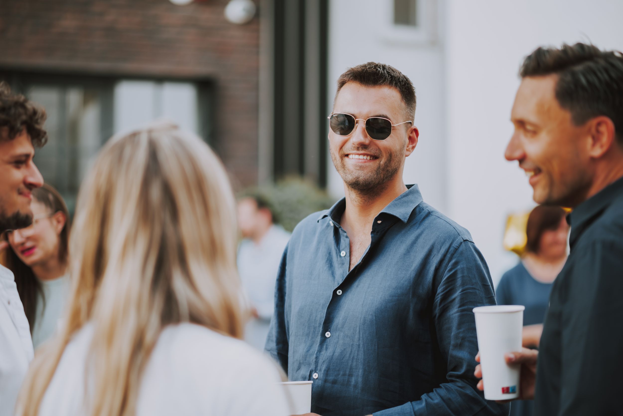 Group of friends chatting and holding drinks at outdoor social gathering.