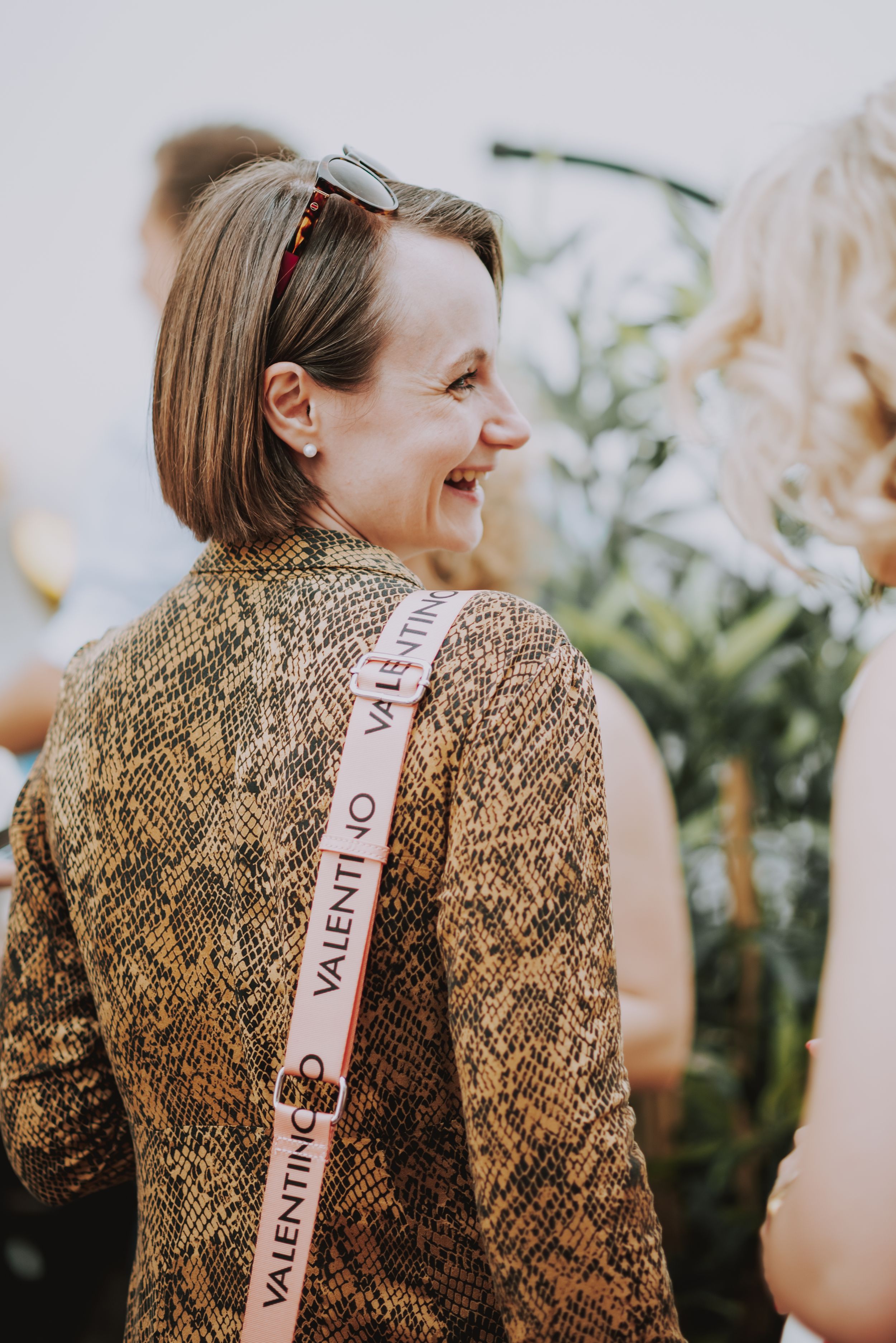 Person in snake print sweater wearing a ribbon strap smiles at an outdoor gathering.