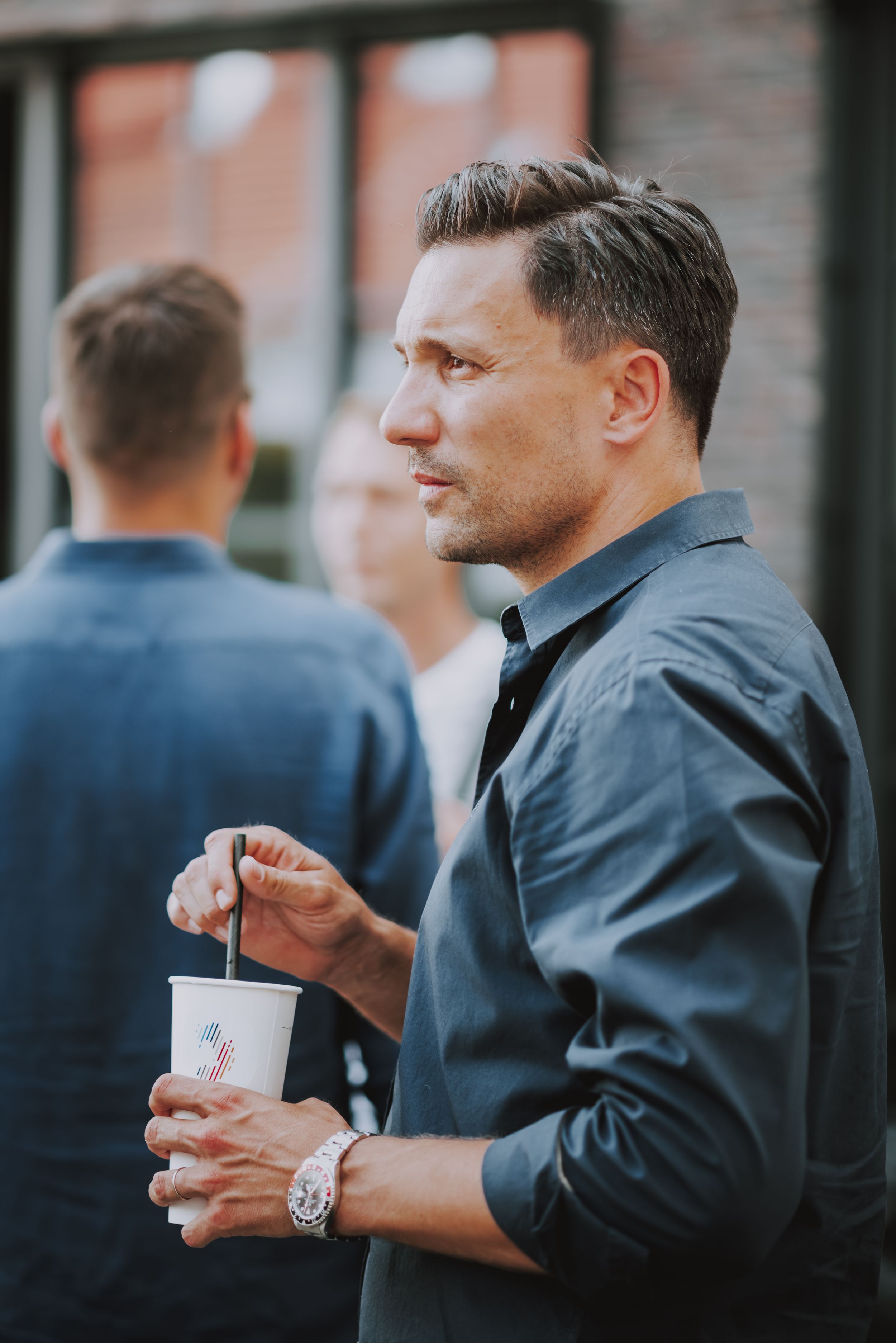 A guest in business casual attire holding a drink at an outdoor networking event.