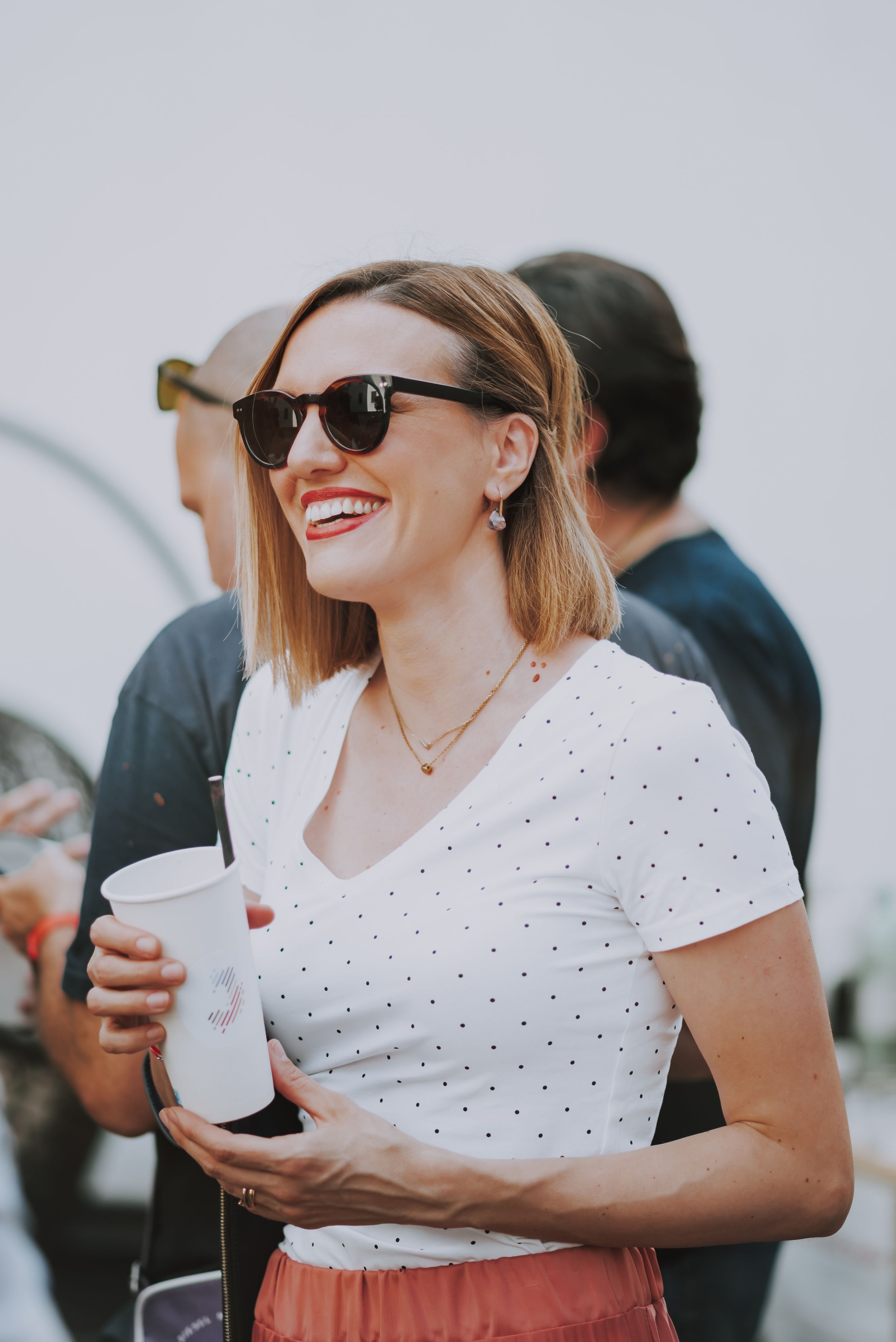 A partygoer in a polka dot shirt and sunglasses enjoying drinks at an outdoor event.