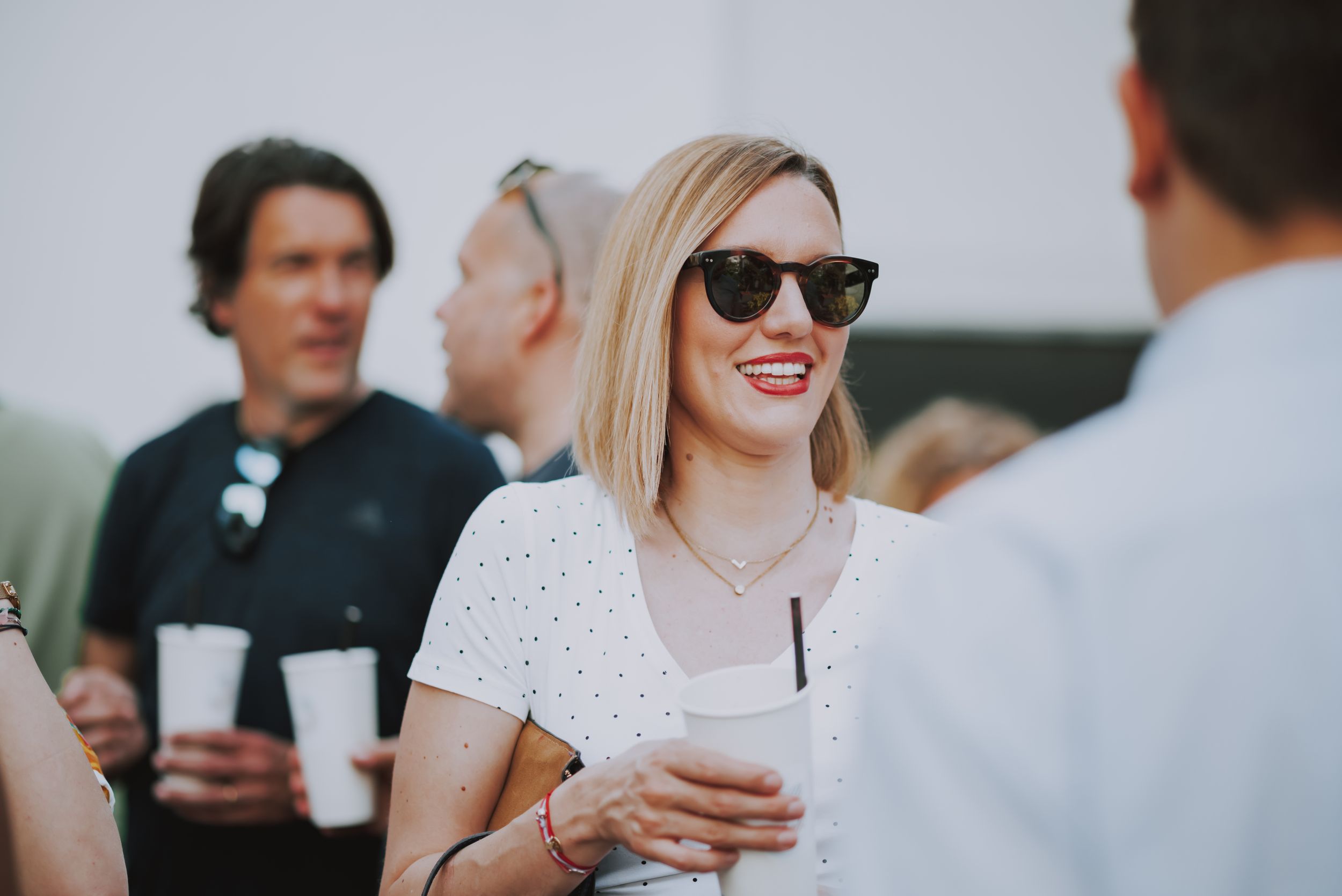 Guest in a white polka dot top and sunglasses socializing at an outdoor event.