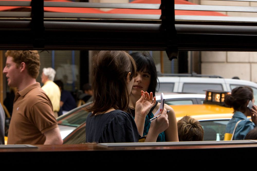 Street scene through window showing people and yellow taxi in urban setting.