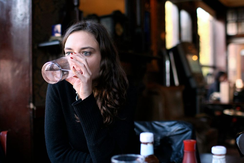 Someone drinks from a wine glass in a cozy restaurant setting.