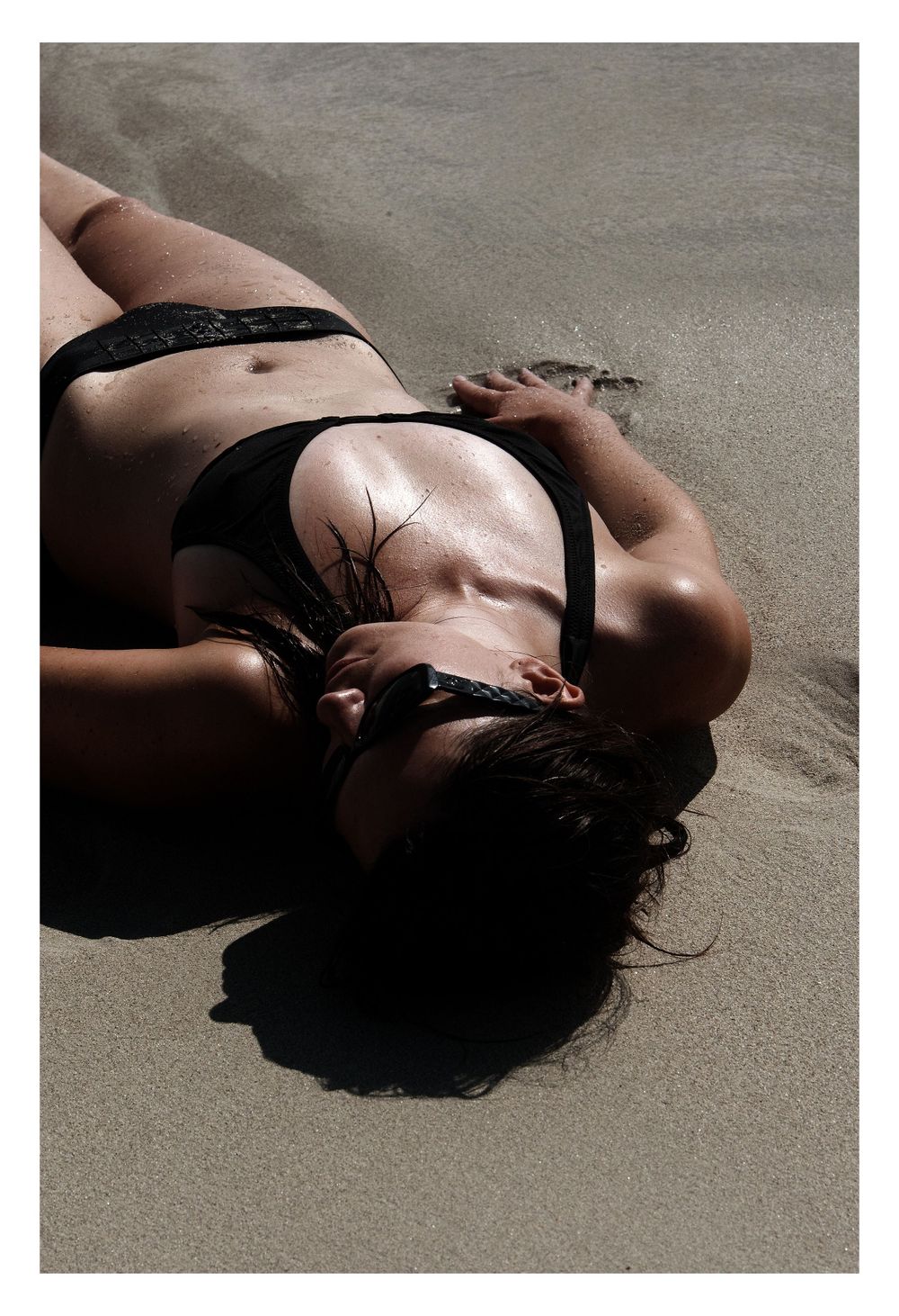 Artistic beach portrait of person in black swimwear lying on sand.