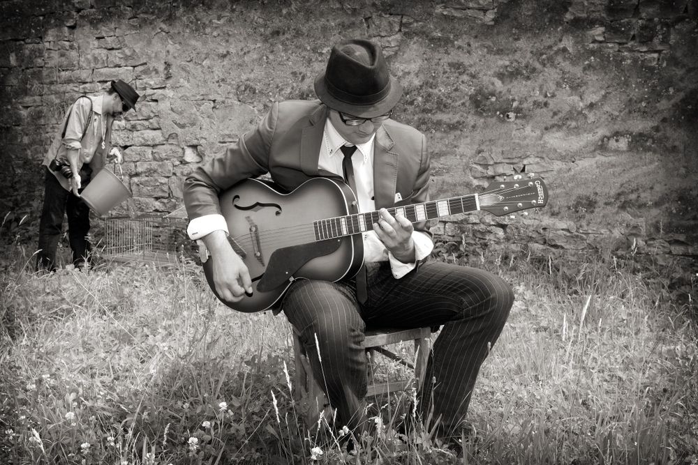 A vintage black and white photo of a musician playing guitar in a rustic outdoor setting.