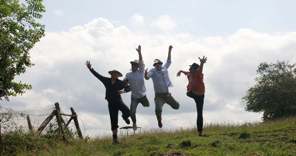 Four people jump joyfully in unison on a hilltop against a cloudy sky.