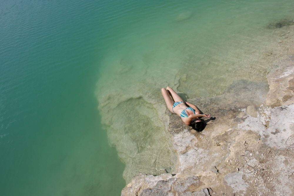 An aerial view of someone swimming in turquoise waters near a rocky shoreline.
