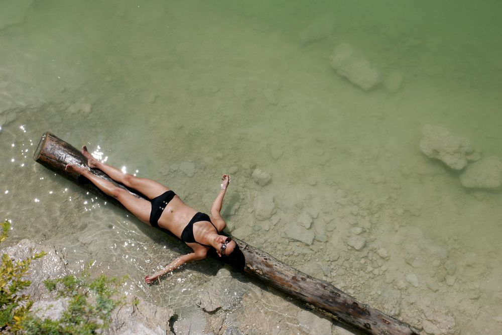 Person relaxing on a log at the edge of turquoise green water.