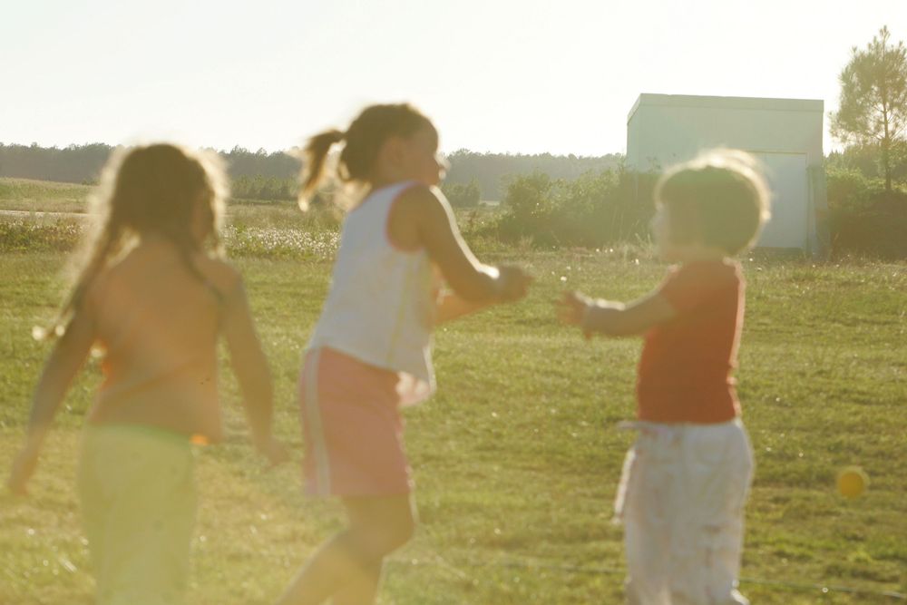 Children playing together in a sunny field at golden hour with a building in the background.