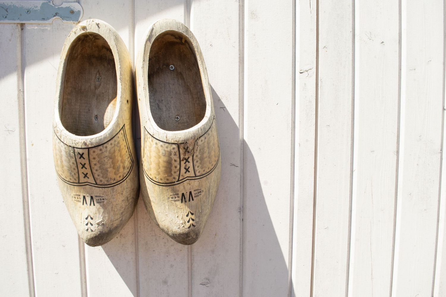 White decorative wooden clogs against a sunlit wall with distinct shadows.