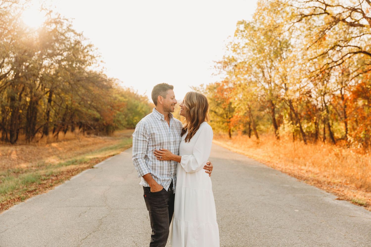 Romantic sunset portrait of a couple on a tree-lined road in autumn.