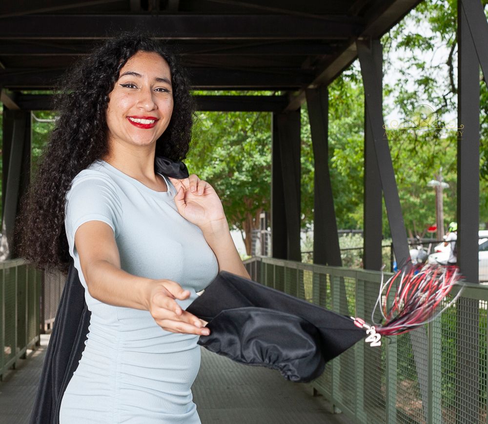 Graduate holds cap while posing in covered outdoor walkway.