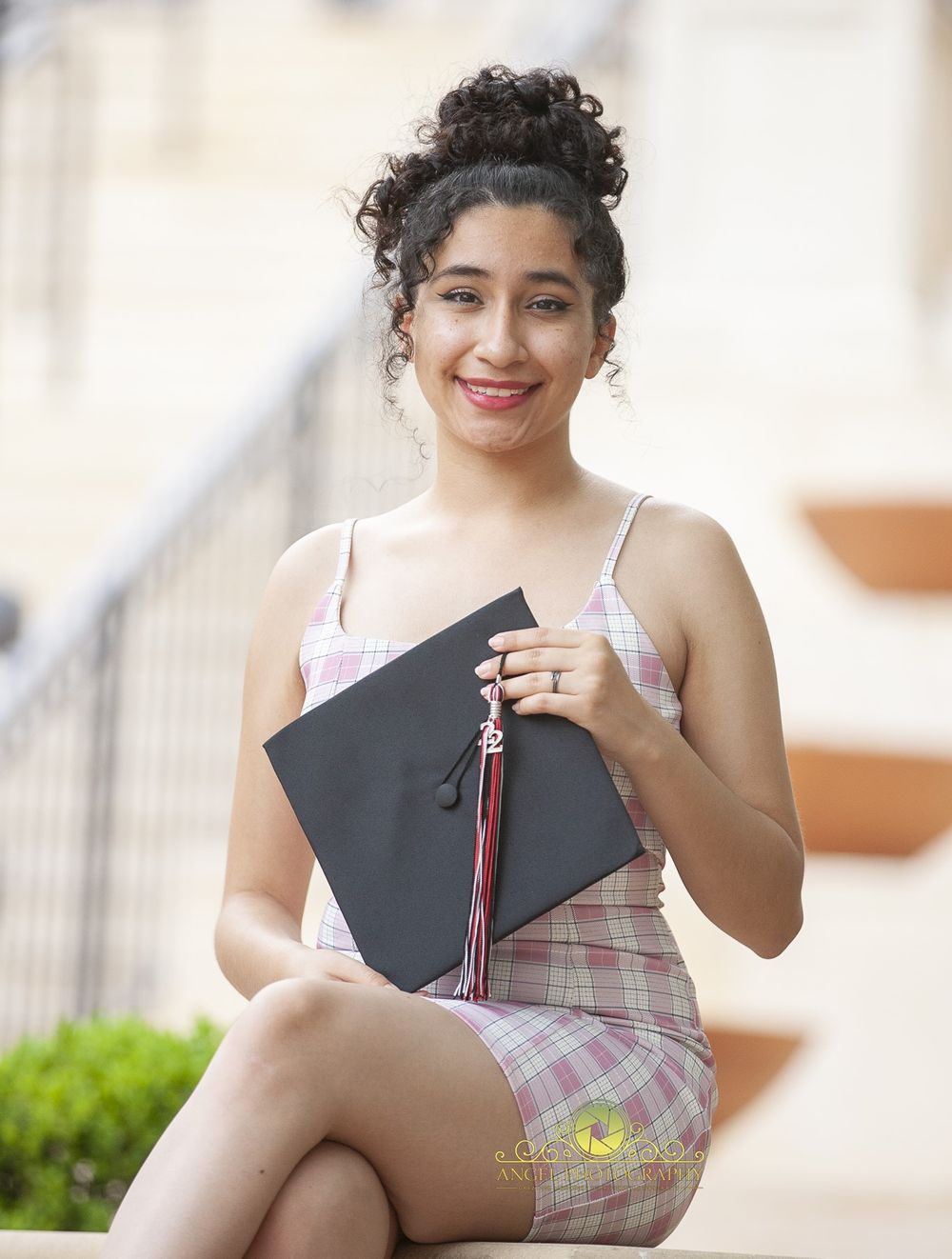 Graduate holds decorated cap while posing on outdoor steps.
