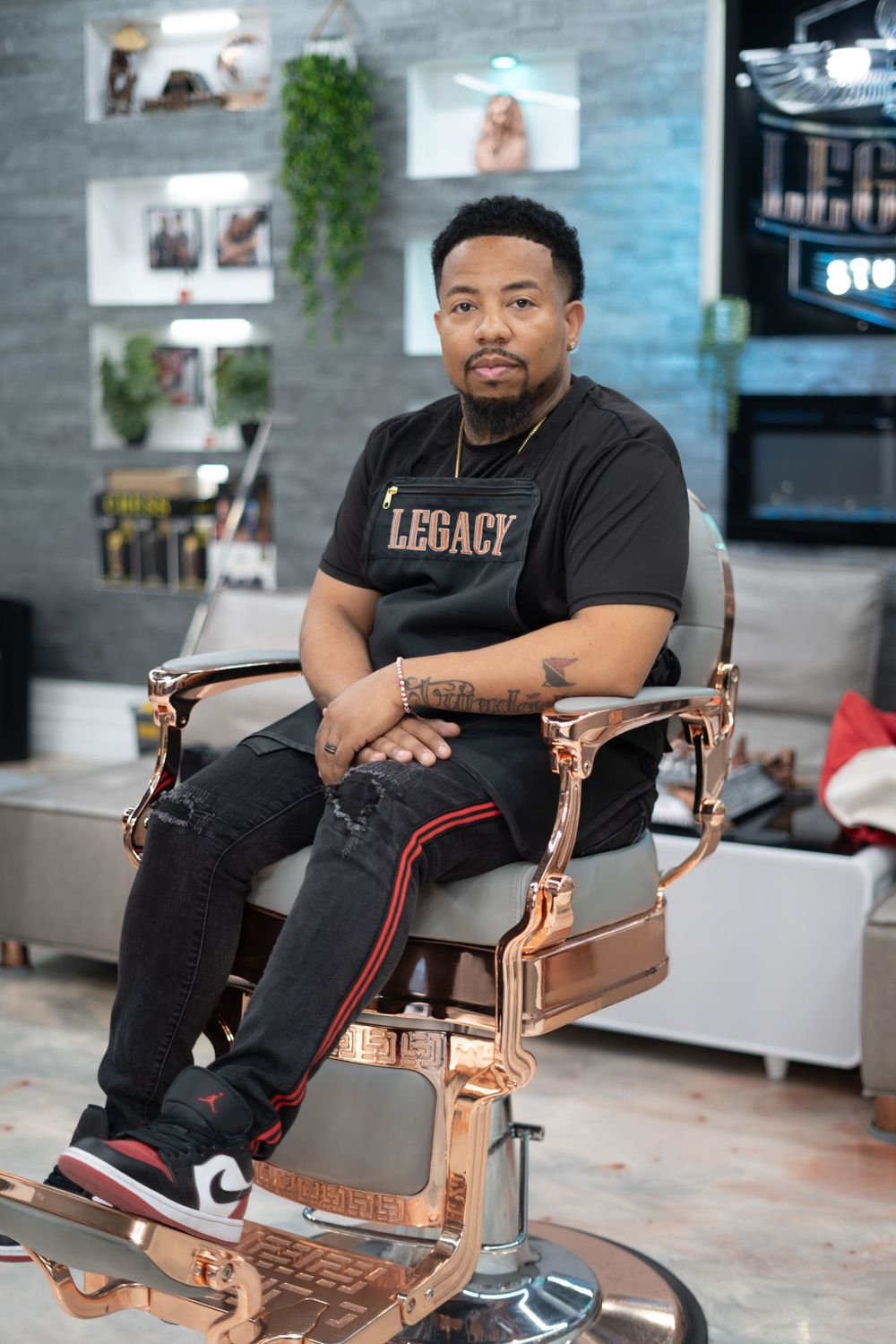 Person wearing a Legacy shirt sits casually in a stylish copper-colored barber chair.