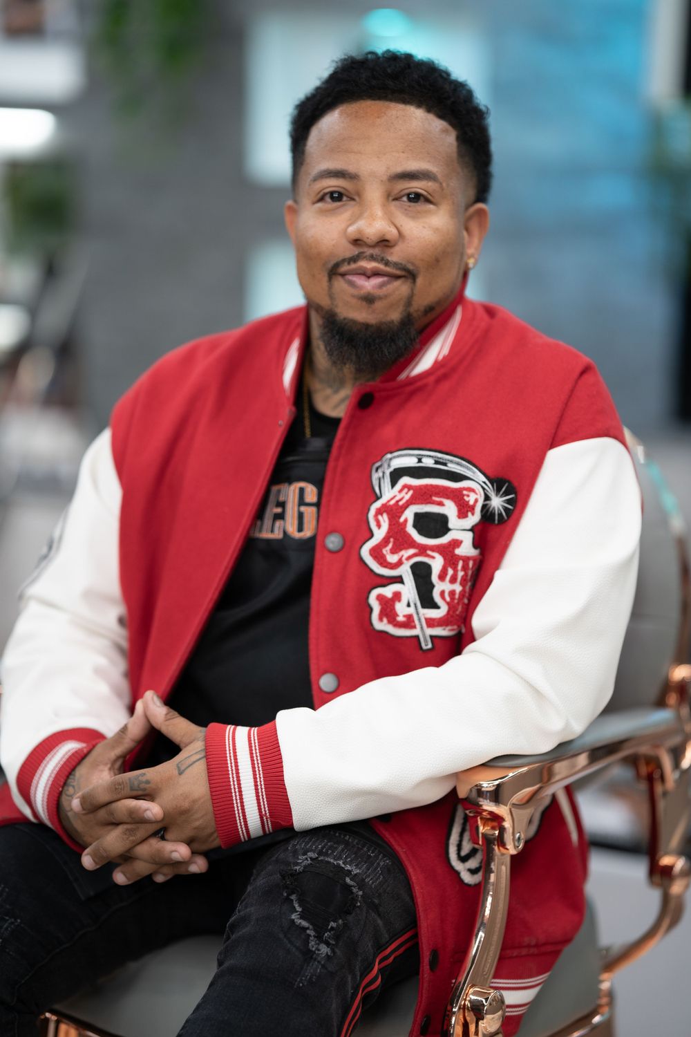 Person in varsity jacket and Legacy shirt posing casually in modern setting.