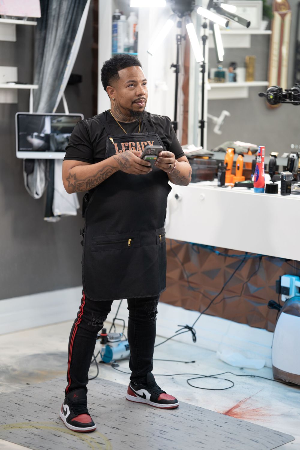 Professional in a black Legacy t-shirt using a mobile phone while standing in a barber shop setting.