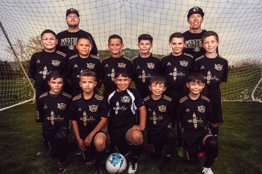 Youth soccer team poses together in black uniforms in front of goal net.