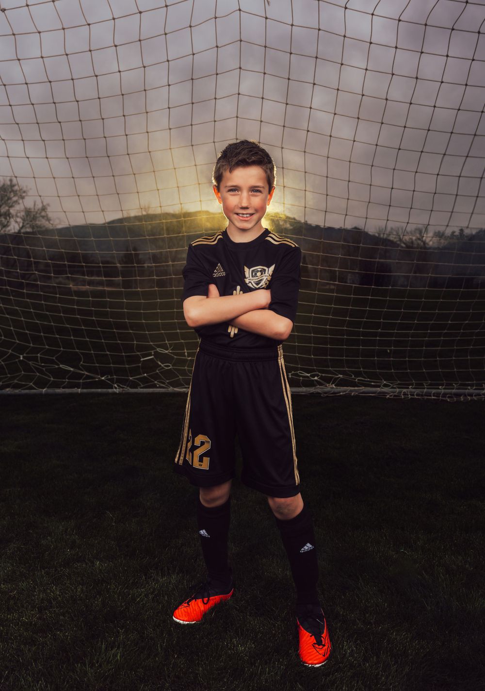 Soccer player in black uniform stands confidently in front of goal net during sunset.