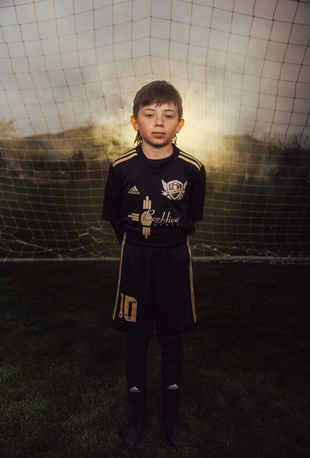 Youth athlete poses in black soccer uniform against glowing sunset and goal net.